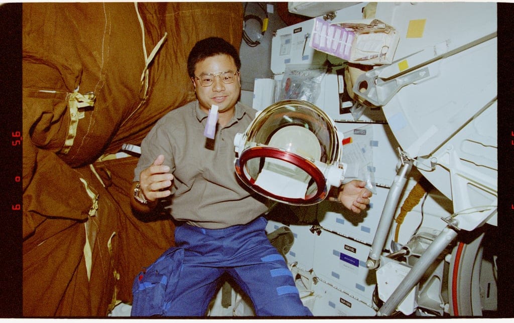 STS-72 Mission Specialist Leroy Chiao floats his extravehicular mobility unit (EMU)/extravehicular activity (EVA) helmet and anti-fog cloth in front of himself in the middeck.